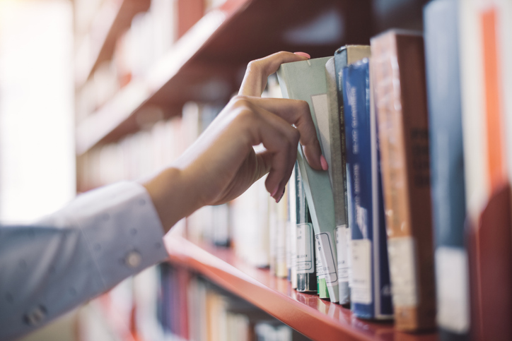 Adult hand reaching for a book from a book shelf